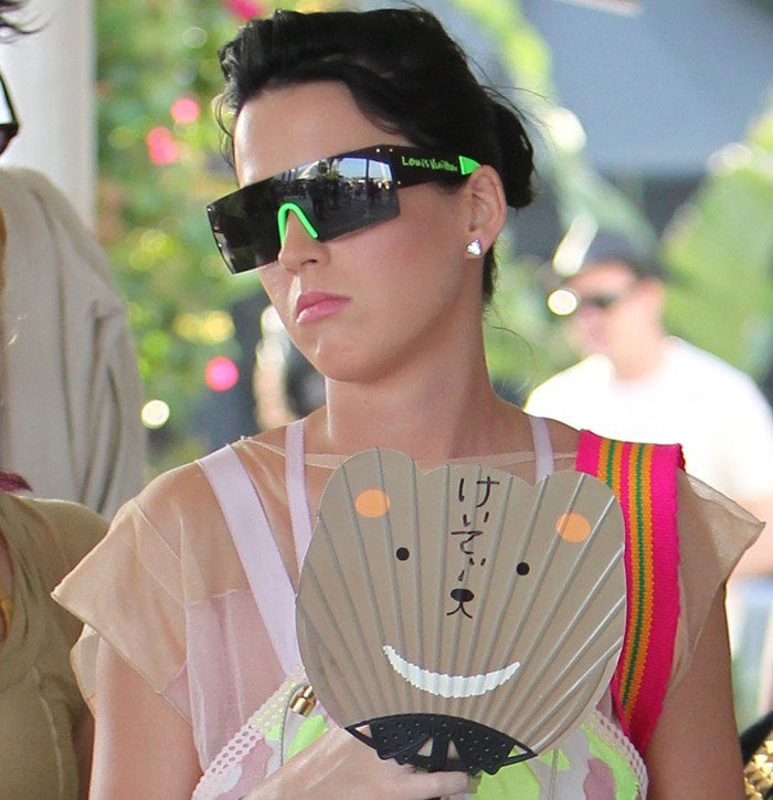Katy Perry keeps cool at Coachella 2010 with futuristic Louis Vuitton sunglasses and a playful Japanese fan, adding a quirky touch to her eclectic festival style