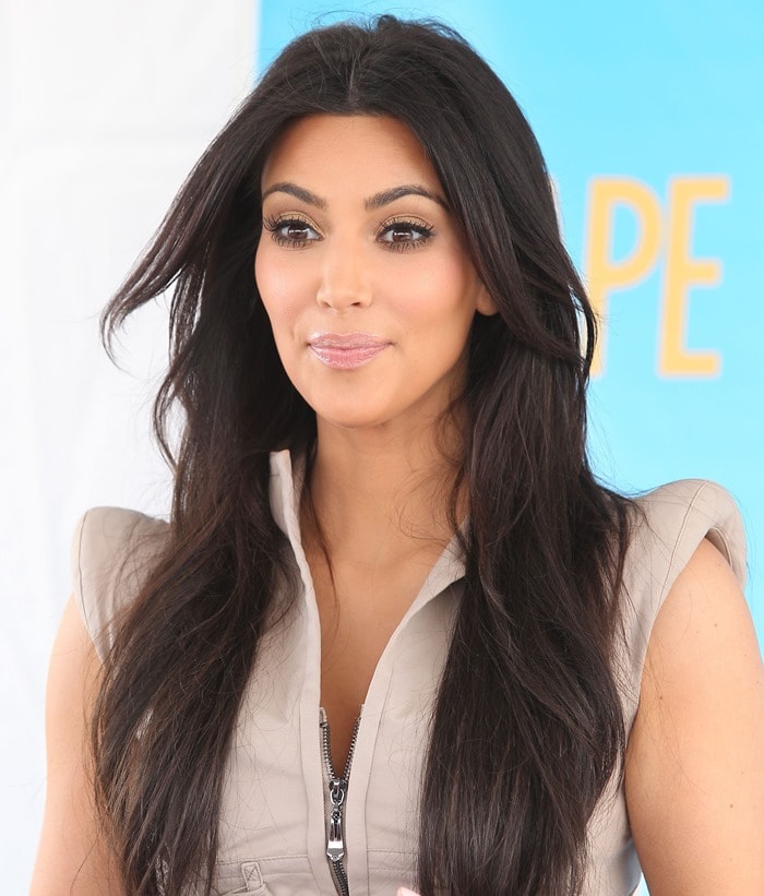 Kim Kardashian showcases sleek, voluminous waves and natural makeup, paired with a chic safari-style dress featuring a standout zipper detail
