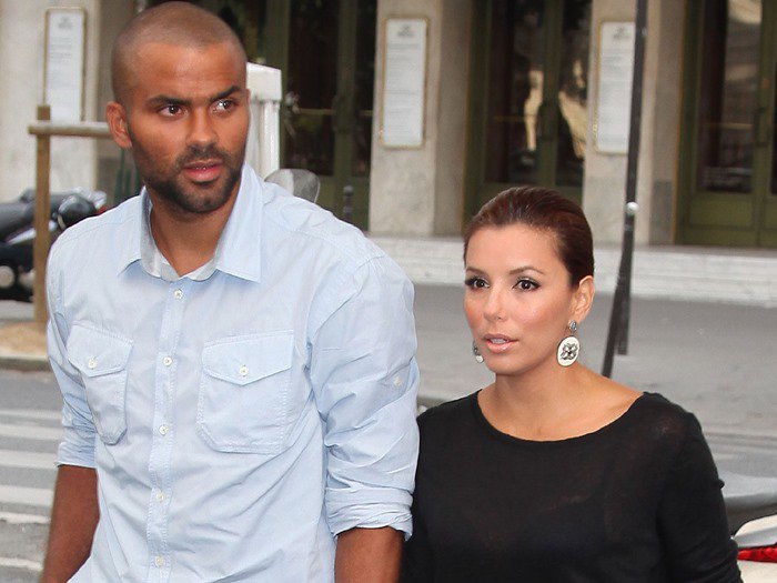 Eva Longoria pairs sleek, pulled-back hair with eye-catching statement earrings, effortlessly complementing her chic all-black outfit while walking with Tony Parker