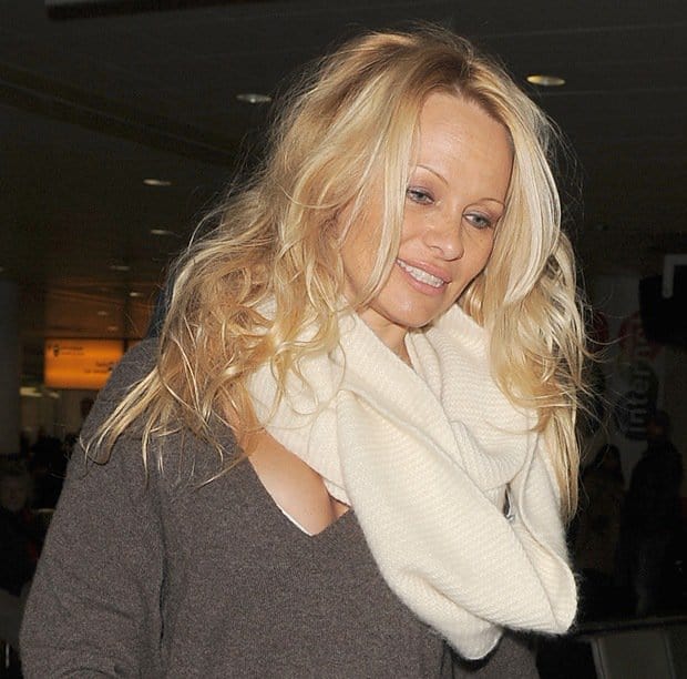 Pamela Anderson keeps it casual yet cozy at Heathrow Airport, pairing a brown sweater dress with a cream scarf for a touch of winter warmth