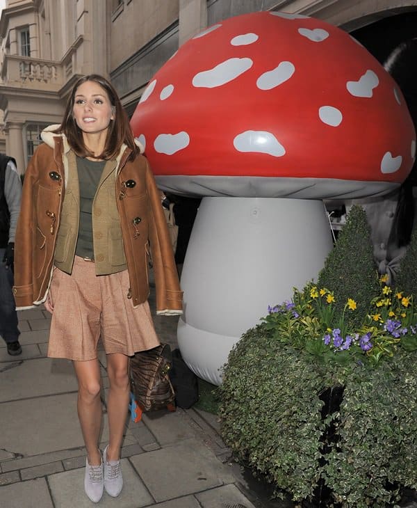 Recreate Olivia Palermo’s chic layered look by pairing a structured olive vest with a shearling-lined leather jacket, a soft pink pleated skirt, and lace-up booties—balancing earthy tones with feminine details for effortless sophistication