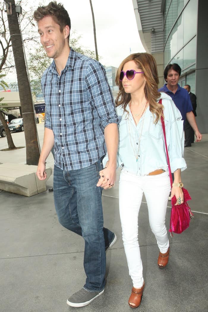 Scott Speer and Ashley Tisdale arrive hand-in-hand at a Los Angeles Lakers game, with Ashley rocking a laid-back denim shirt, white skinny jeans, and studded clogs, while Scott keeps it casual in a plaid shirt, jeans, and grey sneakers