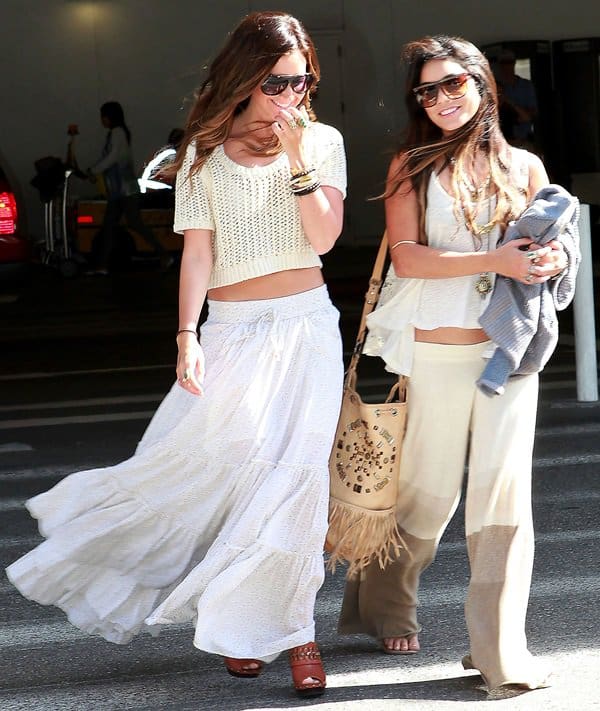 Ashley Tisdale and Vanessa Hudgens arrive at LAX in coordinated bohemian whites, with Tisdale pairing her Free People “Isn’t She” peasant maxi skirt and cropped Harmonica knit with visible Steve Madden Durann clogs, while Hudgens opts for Goddis knit pants, a Blue Life Bare Belly top, and flat sandals