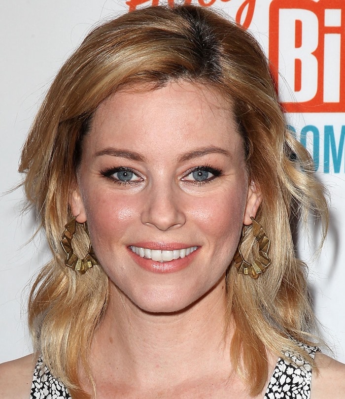 Elizabeth Banks stuns with soft waves and natural makeup, complemented by statement gold earrings, perfectly framing her glowing complexion at the Hollywood Bites Back event