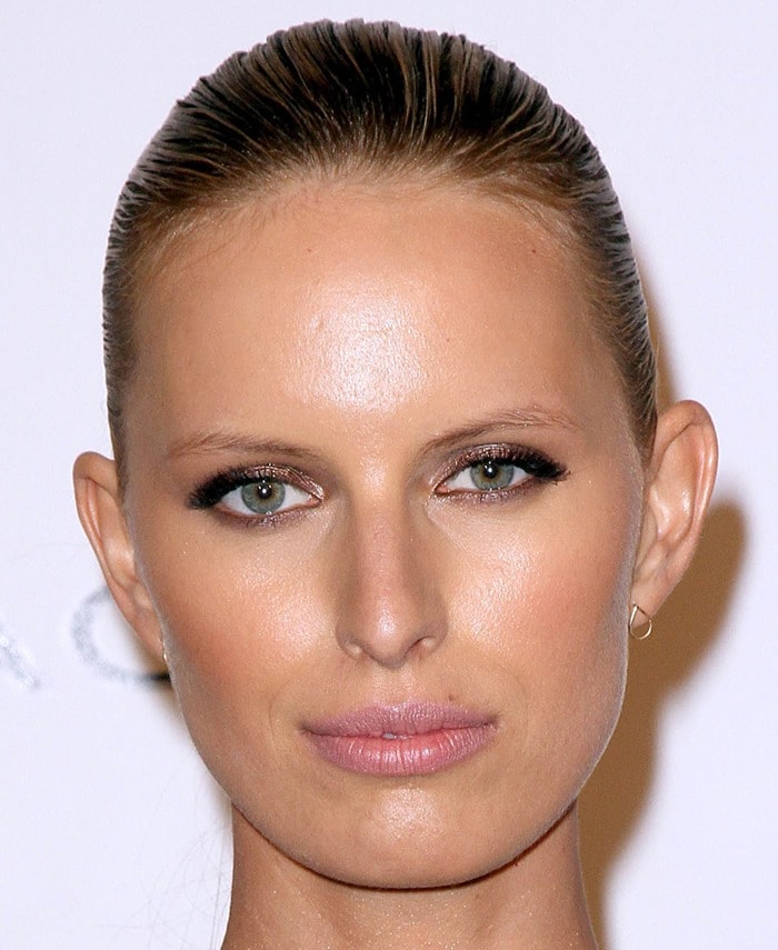 Karolina Kurkova enhances her striking green eyes with soft smoky makeup, complementing her sleek, pulled-back hairstyle and delicate gold hoop earrings