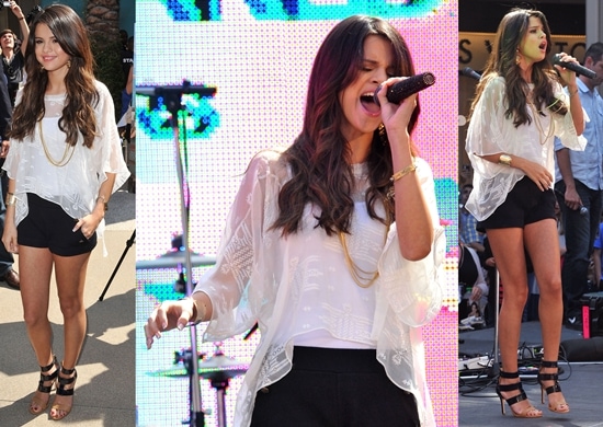 Selena Gomez performing at the Santa Monica Mall Selena Gomez stuns in a breezy white MYNE top, chic black ASOS shorts, and statement Tory Burch 'Danielle' sandals, effortlessly blending casual elegance with stage-ready glamour
