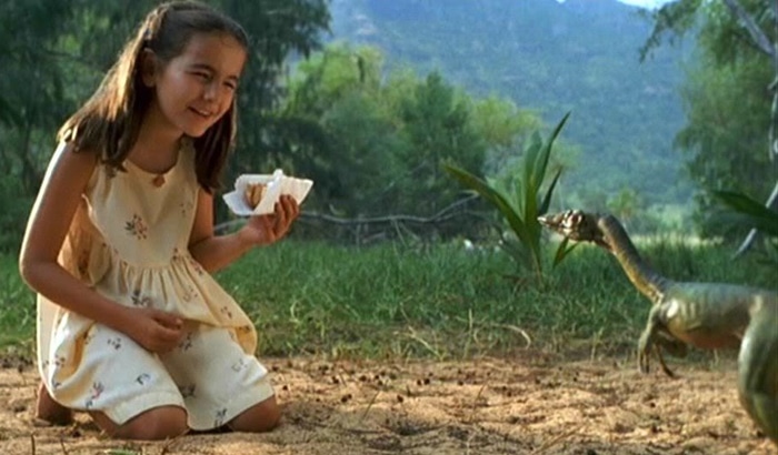 Camilla Belle, dressed in a sleeveless cream sundress with floral embroidery, mistakes a Procompsognathus for a harmless lizard in The Lost World: Jurassic Park