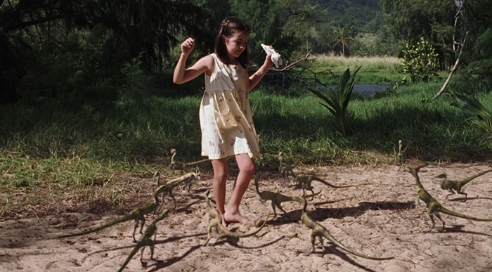 Wearing a pale yellow sundress with playful embroidered details, Camilla Belle’s character Cathy Bowman is ambushed by Compsognathus in The Lost World: Jurassic Park