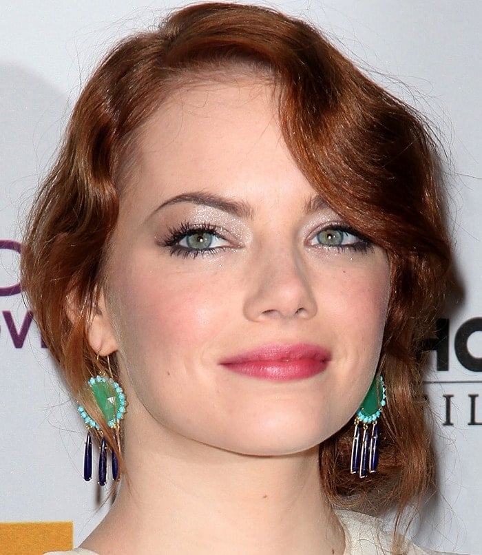 Emma Stone stuns with shimmering silver eye makeup that highlights her green eyes, while her bold turquoise and navy earrings add a vibrant pop of color to her look