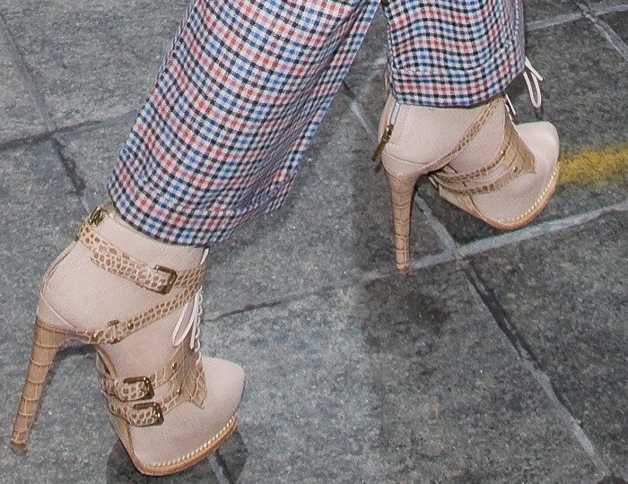 Jennifer Lopez’s Dior Guetre booties combine crocodile-embossed harness straps, corset-style lacing, and towering wrapped stiletto heels beneath tailored plaid trousers