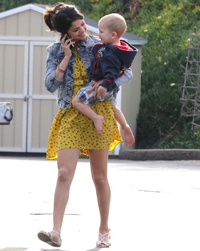On February 17, 2012, in Malibu, Selena Gomez was spotted wearing a Topshop Daisy Dogs shirtdress, a Heritage 1981 acid wash denim jacket, and Urban Outfitters Twisted T-Strap sandals