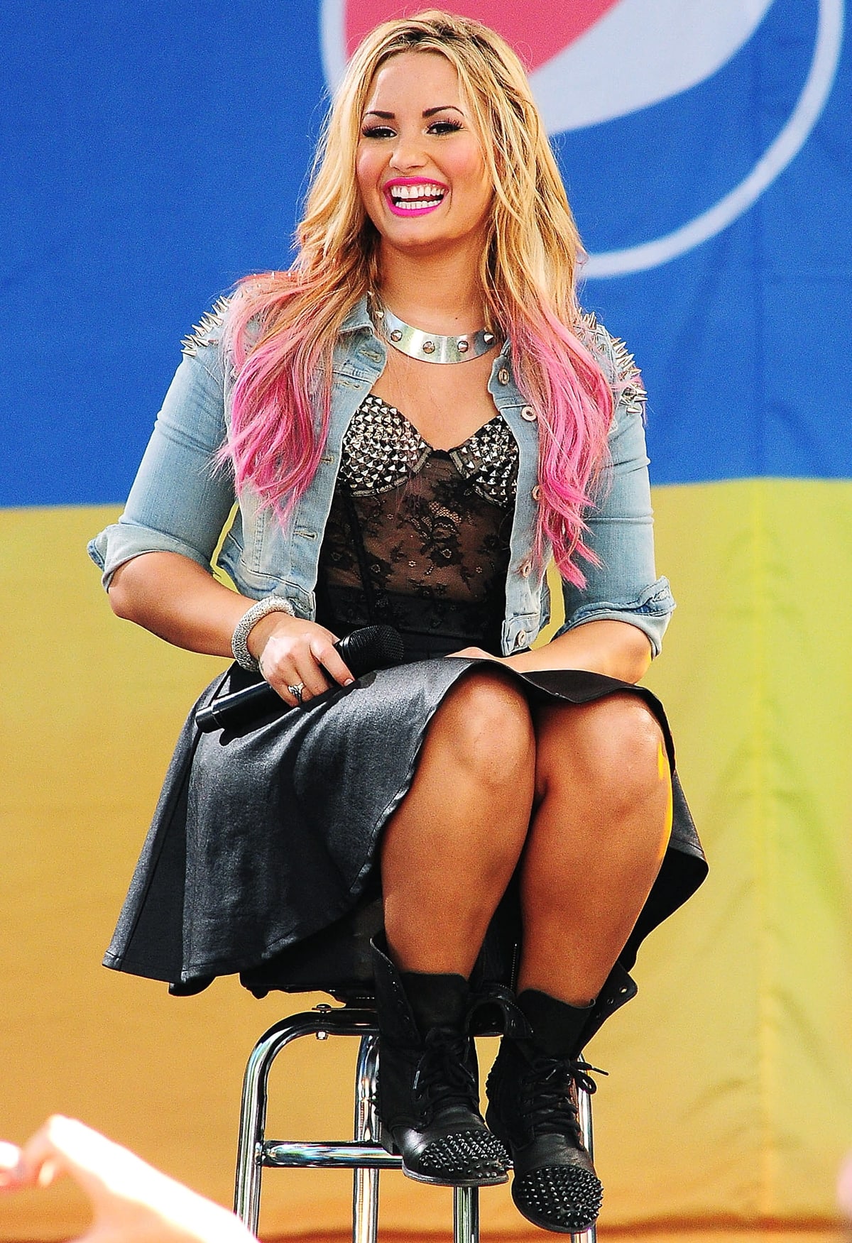 Demi Lovato rocks an edgy-chic look in a studded floral lace bustier, black leather skirt, and a cropped denim jacket, completing the ensemble with black studded combat boots for a bold, statement-making finish