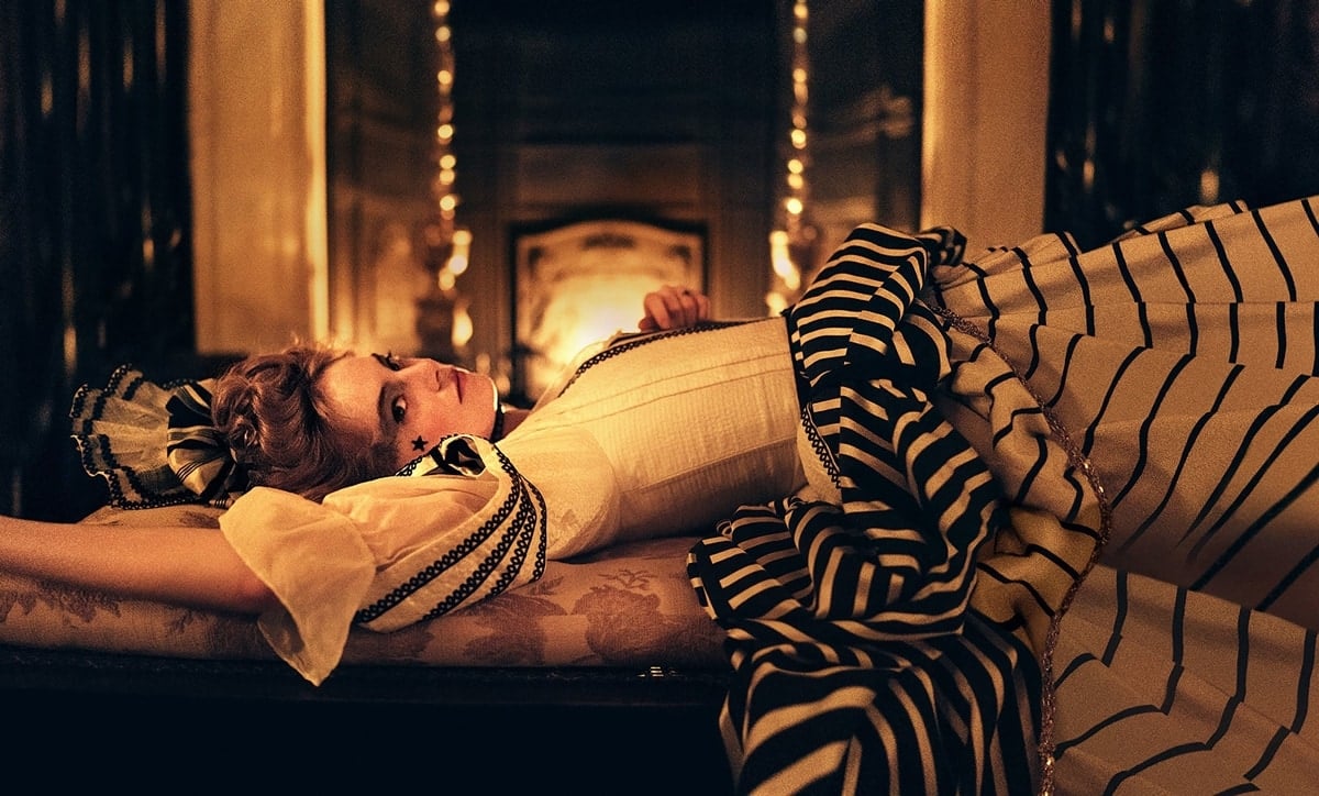 Emma Stone as Abigail Hill in the 2018 period black comedy The Favourite, wearing an elaborate striped 18th-century costume with puffed sleeves and ribbon details—a striking look that underscores the film’s opulent yet irreverent take on historical fashion
