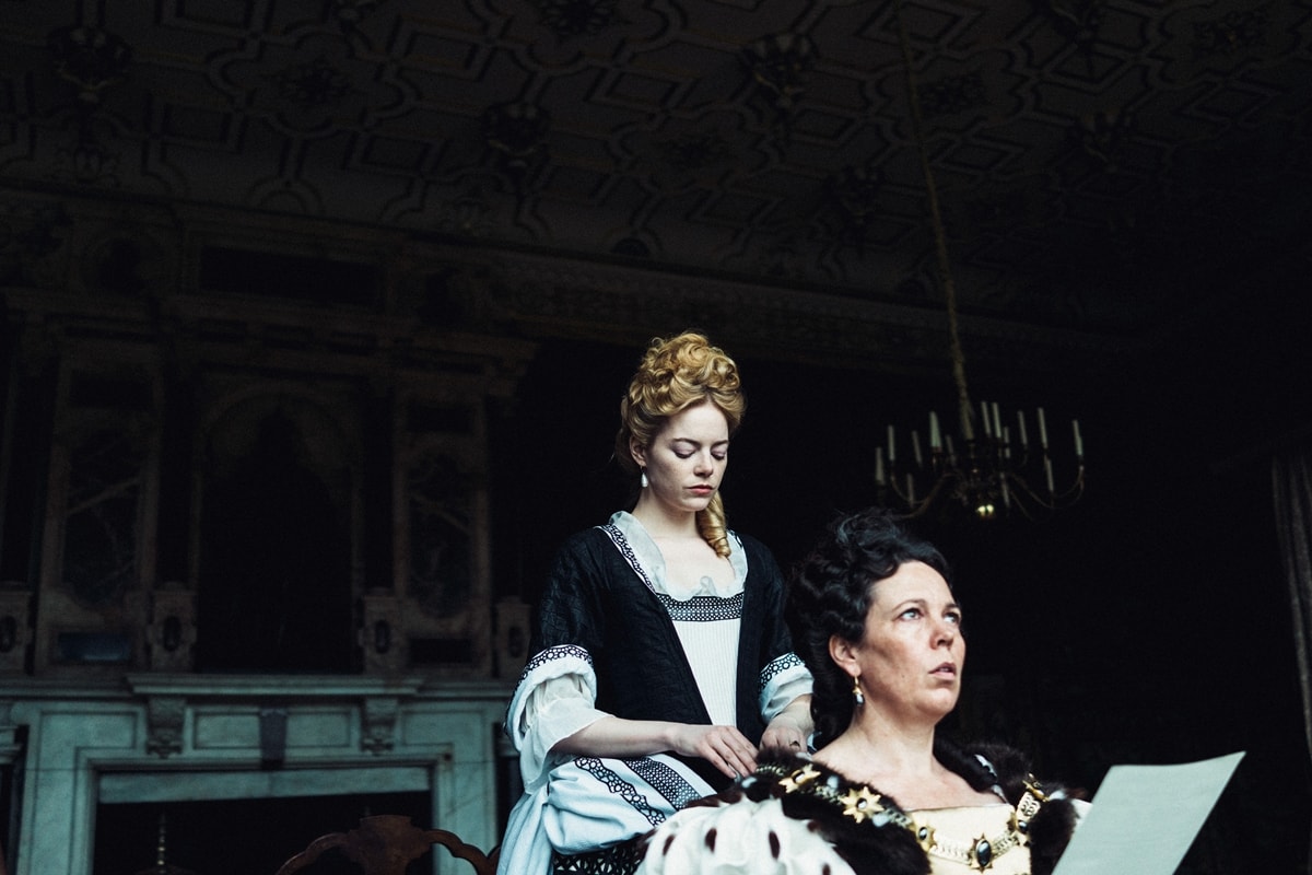Olivia Colman as Queen Anne and Emma Stone as Abigail Hill in The Favourite, both dressed in richly detailed 18th-century gowns that showcase the film’s opulent approach to period costume design