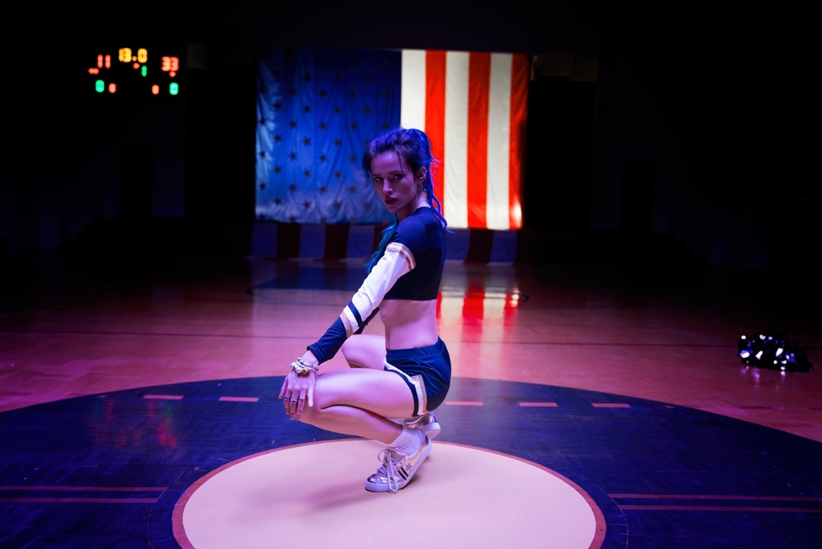 Bella Thorne strikes a fierce pose as Reagan Hall in Assassination Nation (2018), sporting a bold cheerleader-inspired outfit paired with metallic silver athletic sneakers that complement her edgy, rebellious character