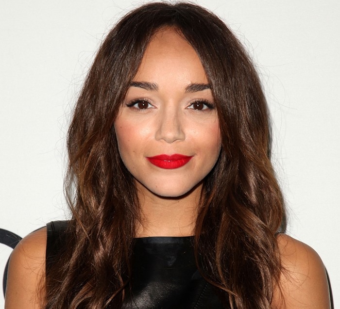 Ashley Madekwe showcases soft, tousled waves with a center part, complemented by flawless makeup featuring bold red lips, defined brows, and subtle contouring for a polished yet effortless look