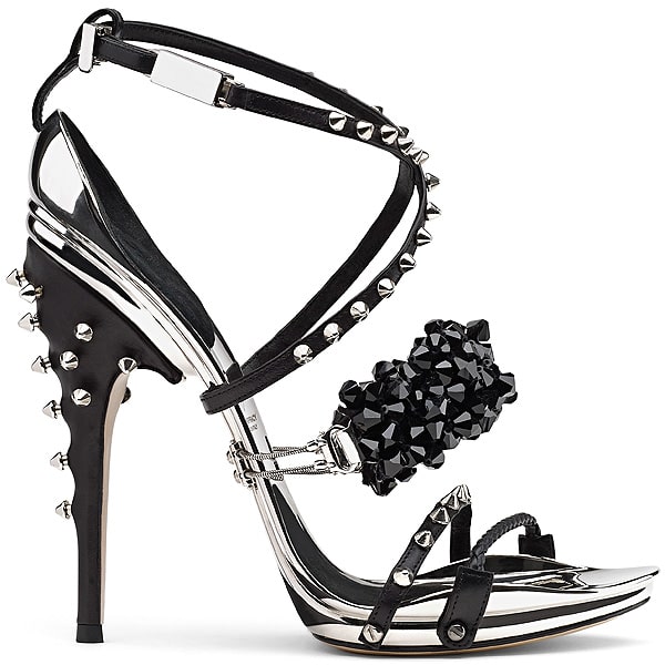 Gianluca Tamburini Vivienne Vivienne pairs punk edge with precision engineering—featuring spiked black leather straps, a faceted crystal cluster, and a chrome-accented stiletto heel with metallic studs