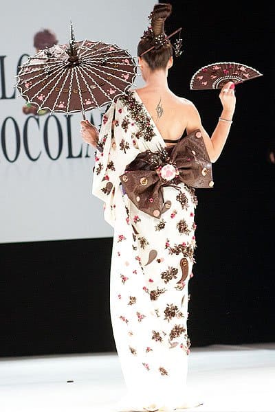 The Chocolate Dress Fashion Show Natasha St-Pier elegantly showcases a chocolate-crafted kimono, complete with a chocolate parasol, fan, and obi bow, blending tradition with confectionery art