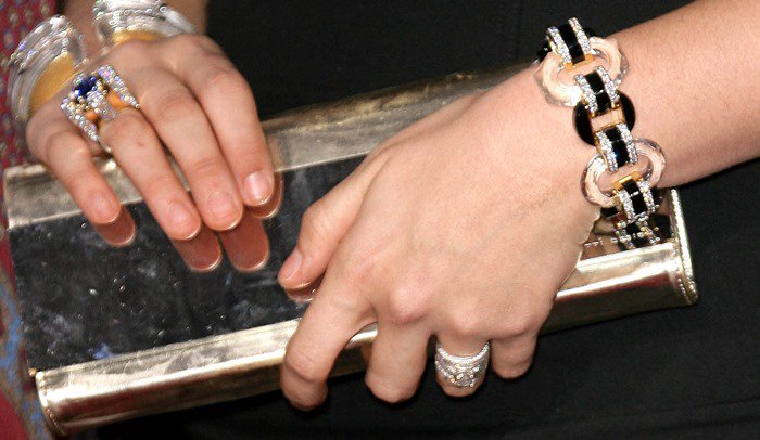 Hillary Scott accessorizes her all-black look with statement jewelry by David Webb, stacking bold rings and a chain-link bracelet alongside a sleek gold clutch for a polished red-carpet finish