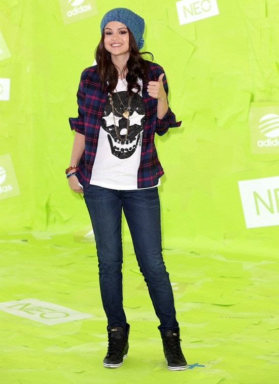 Selena Gomez Selena Gomez announces new global partnership with iconic fashion brand at Adidas 'NEO' news conference and photocall Los Angeles, California Dressed in Adidas NEO, Selena Gomez combines a white skull shirt, blue jeans, and a checkered shirt-jacket with black kicks at the Los Angeles event
