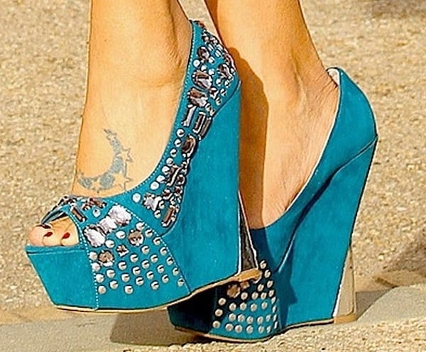 Bai Ling shows off her foot tattoo in vibrant turquoise Promise “Lux” peep-toe wedges, embellished with silver studs and set on dramatic 6-inch wedge heels