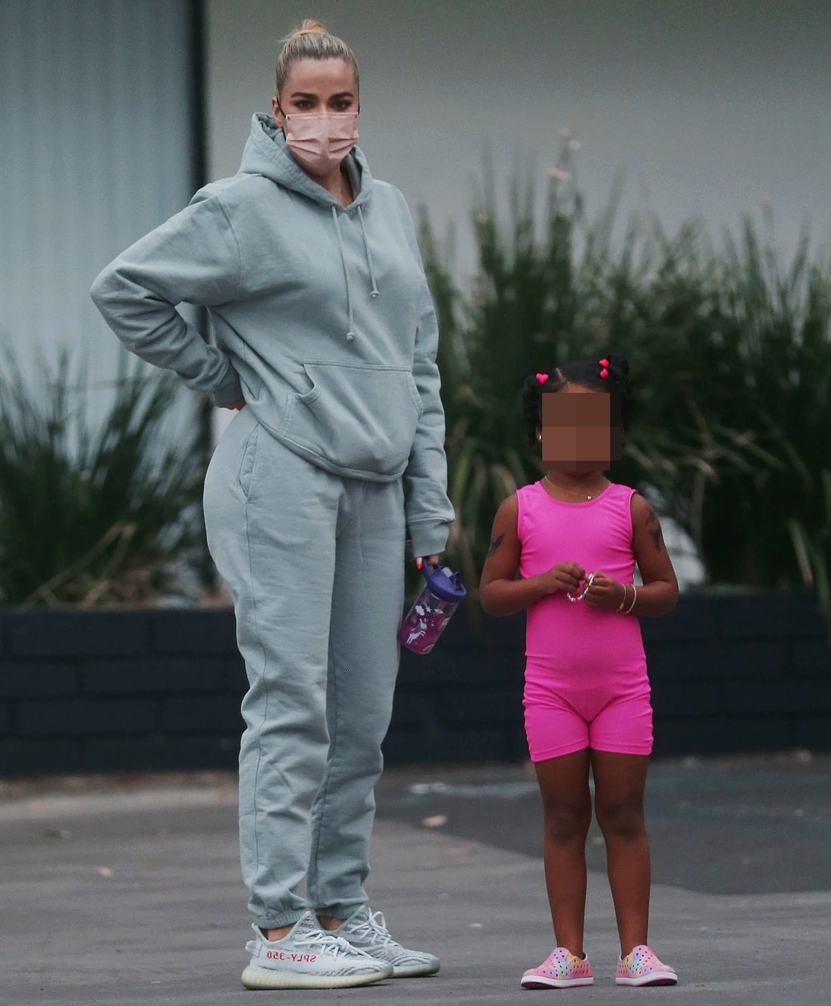 Balancing oversized loungewear with streamlined sneakers, Khloé Kardashian keeps the look grounded with low-profile Yeezys while her daughter’s bright pink outfit adds a playful pop of color