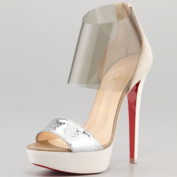Christian Louboutin’s “Dufoura” sandal in nude and silver pairs a sculptural PVC ankle shield with a towering red-soled stiletto and stacked platform for dramatic architectural impact