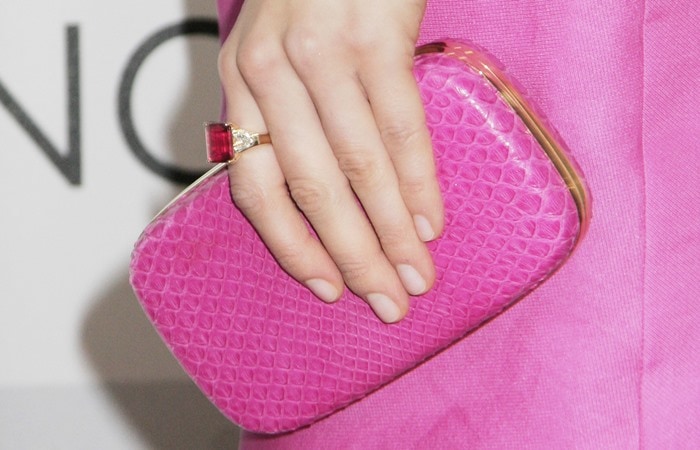 Georgia King toting a pink clutch manicure ring Georgia King complements her vibrant pink dress with a matching textured pink clutch, showcasing a subtle nude manicure and a striking ring featuring a large red gemstone accented with smaller white stones