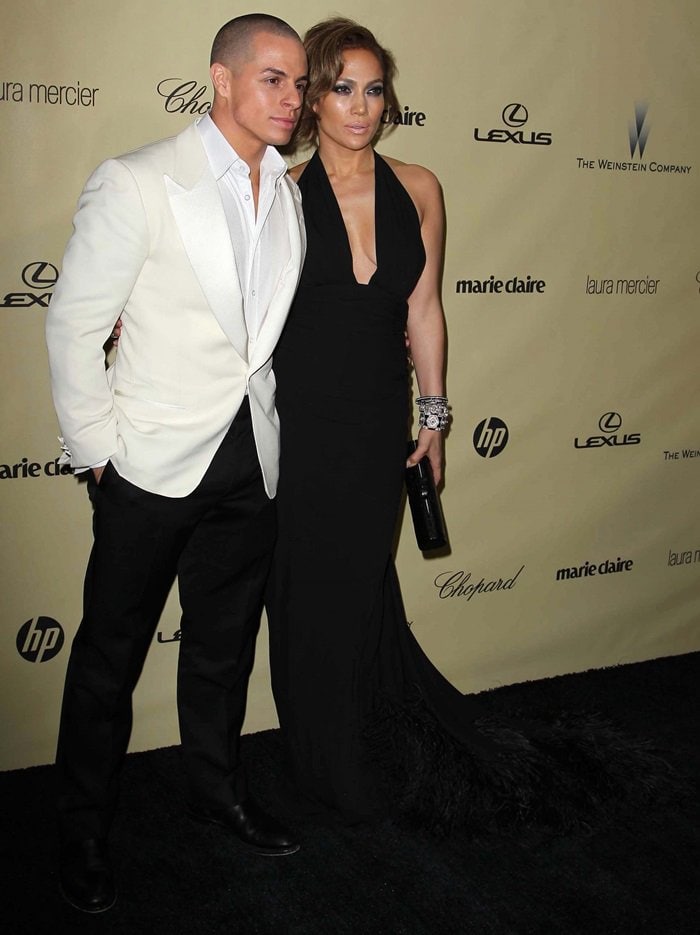 Jennifer Lopez exudes Old Hollywood glamour in a plunging black gown paired with sparkling jewelry, standing alongside Casper Smart in a crisp white tuxedo