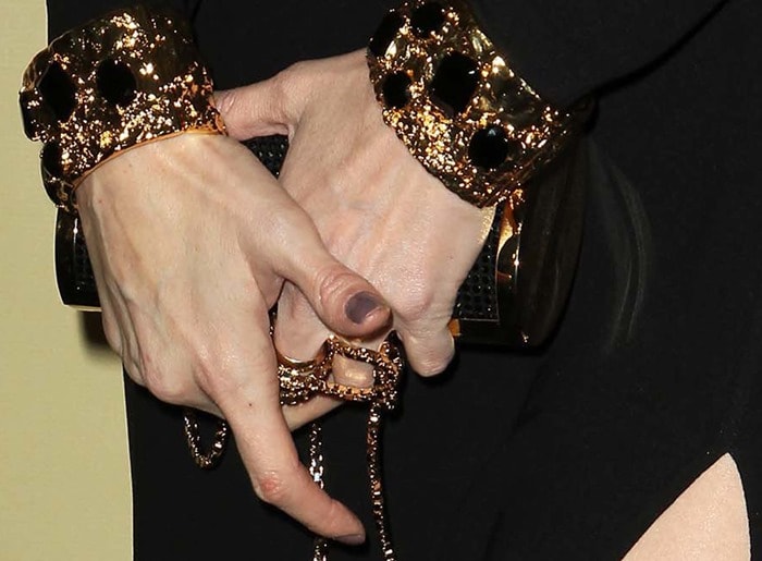 Paz Vega accessorizes her chic black gown with a bold manicure featuring deep plum nails, a sleek black clutch with a chain detail, and striking gold bracelets adorned with black accents