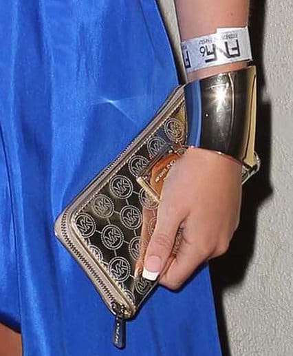 Alli Simpson’s gold Michael Kors “Mirror Monogram” clutch infuses her cobalt-blue look with a polished, high-shine finish