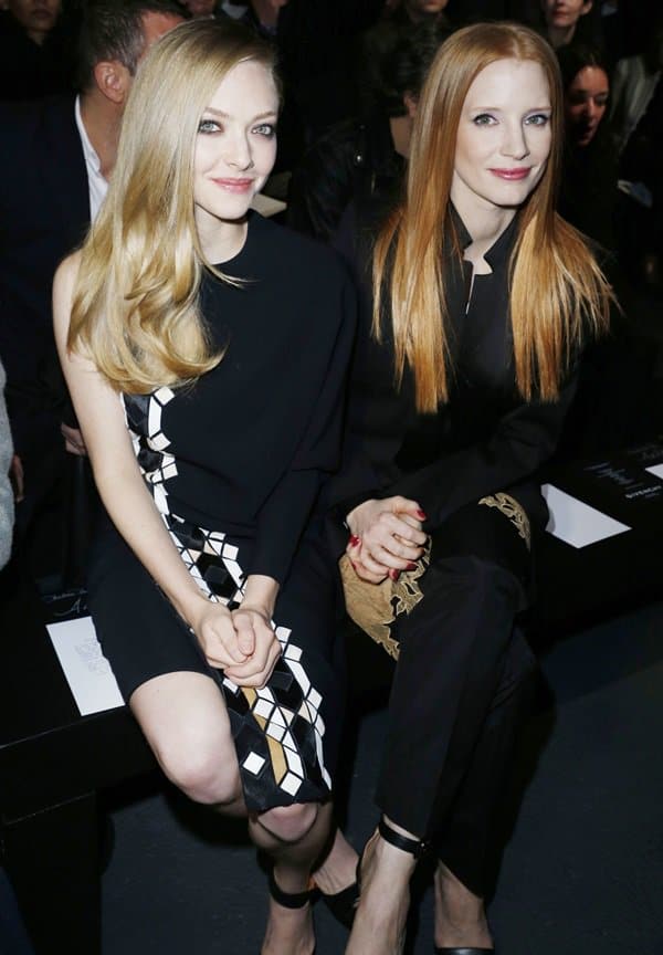 Amanda Seyfried and Jessica Chastain sit front row at the Givenchy Fall/Winter 2013 show, with Amanda in a geometric black-and-white dress and ankle-strap stilettos, and Jessica in a sleek black suit featuring gold lace accents and peep-toe heels