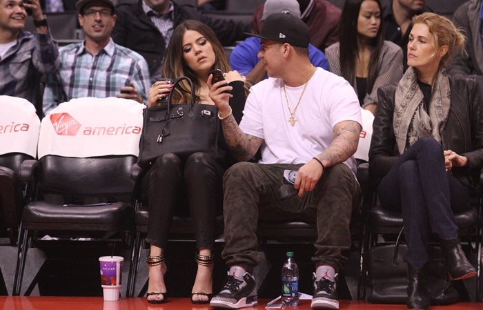 Khloé Kardashian and Rob Kardashian are pictured courtside, with Khloé holding her Hermès Birkin bag and Rob sporting casual streetwear