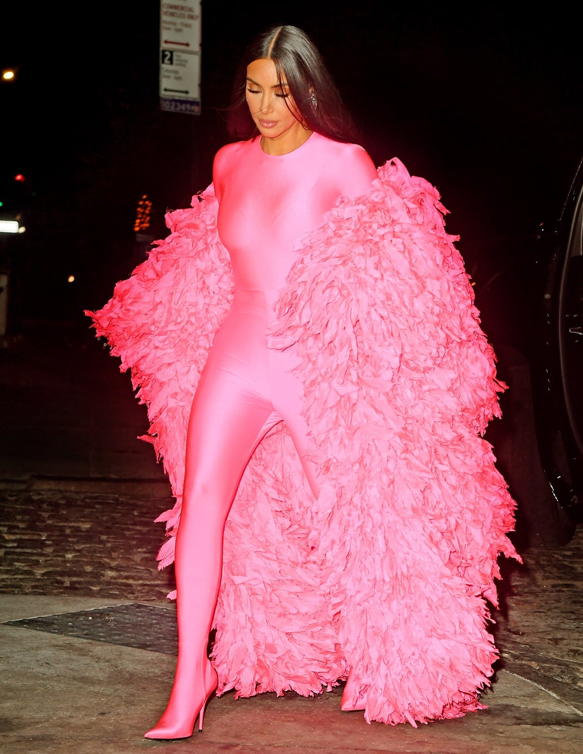 Kim Kardashian steps onto the New York City sidewalk in her head-to-toe pink Balenciaga look, pairing the sleek catsuit with matching Knife boots and an oversized feathered coat