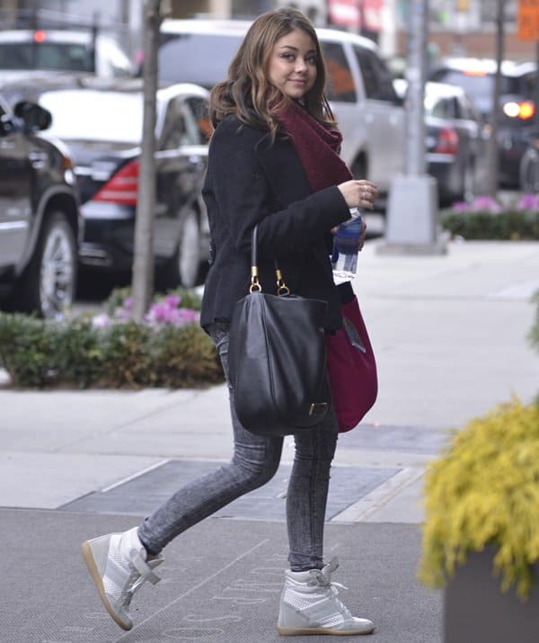Sarah Hyland exudes young fashion flair in a black pea coat, faded skinny jeans, and trendy wedge sneakers on the streets of SoHo, NYC