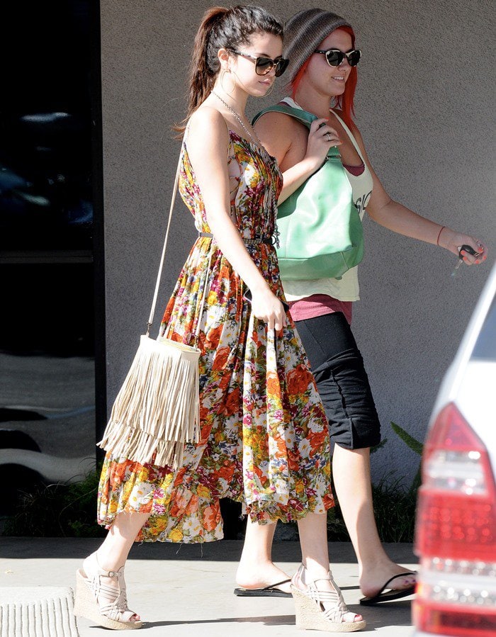 Selena Gomez was spotted in Encino on February 28, 2013, styled in an FP One criss-cross florals maxi dress in ivory, complemented by Tory Burch Nadia wedge sandals, and accessorized with a McFadin Sundance fringe bag in stone