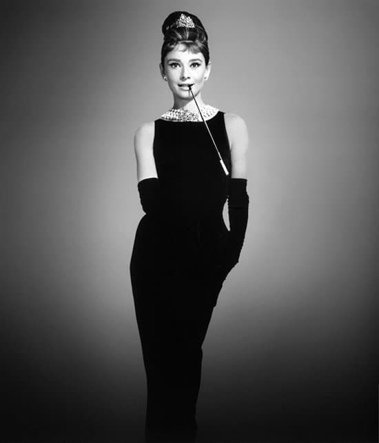 Audrey Hepburn epitomizes timeless elegance as Holly Golightly in a sleek black Givenchy gown, opera gloves, a sparkling tiara, and her signature cigarette holder
