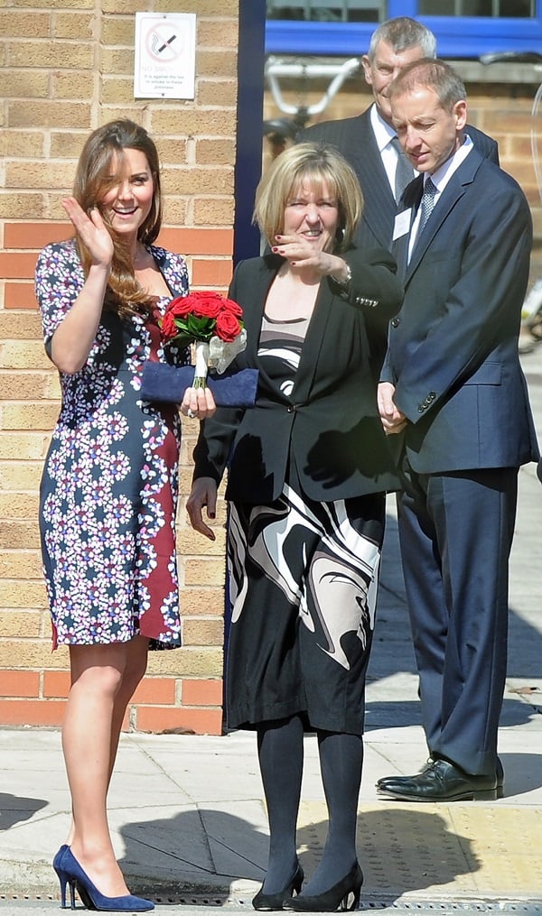 Duchess Kate gracefully dons a captivating floral Erdem 'Sophia' dress with quarter sleeves, exquisitely paired with a Stuart Weitzman for Russell Bromley navy suede Muse clutch