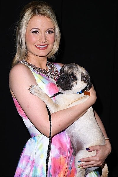 Holly Madison, dressed in her vibrant Alice + Olivia outfit, happily holds a charming dog at the animal-themed event