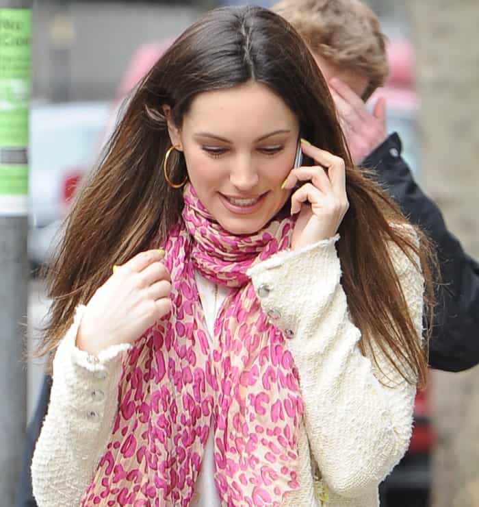 Kelly Brook brightens her casual London look with a pink leopard-print scarf layered over a white knit blouse, adding a playful pop of color to her understated ensemble