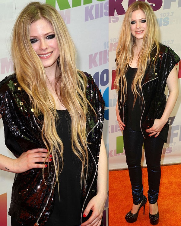 Avril Lavigne rocks her signature edgy-glam style in a sequined biker vest layered over an all-black ensemble, finishing the look with studded platform pumps for a bold, rebellious touch