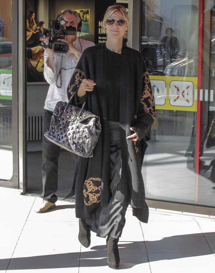 Heidi Klum keeps it effortlessly chic in layered black separates, knee-high suede boots, and oversized sunglasses, finishing her look with a statement Hermès Birkin snakeskin bag while arriving at Berlin’s Tegel Airport