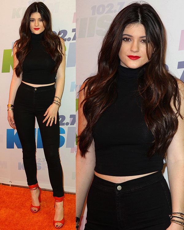 Kylie Jenner serves a sleek monochrome moment in a black cropped turtleneck and high-waisted skinny jeans, adding a bold pop of color with striking red Alexander Wang 'Aminata' sandals