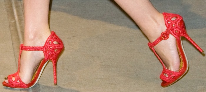 Kylie Minogue adds a bold pop of color to her look with red Dolce Gabbana lace T-strap sandals, featuring intricate cutout details and a chic stiletto heel