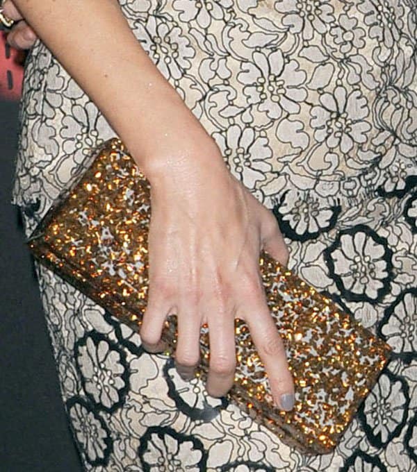 Lake Bell carries a gold-and-black Edie Parker “Flavia” clutch that adds texture and vintage-inspired sparkle to the monochrome lace look