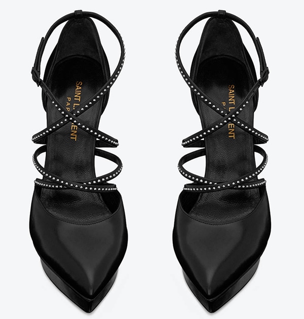 The Saint Laurent “Janis” studded platform pump features sleek crisscross straps, a beveled platform, and a towering stiletto heel