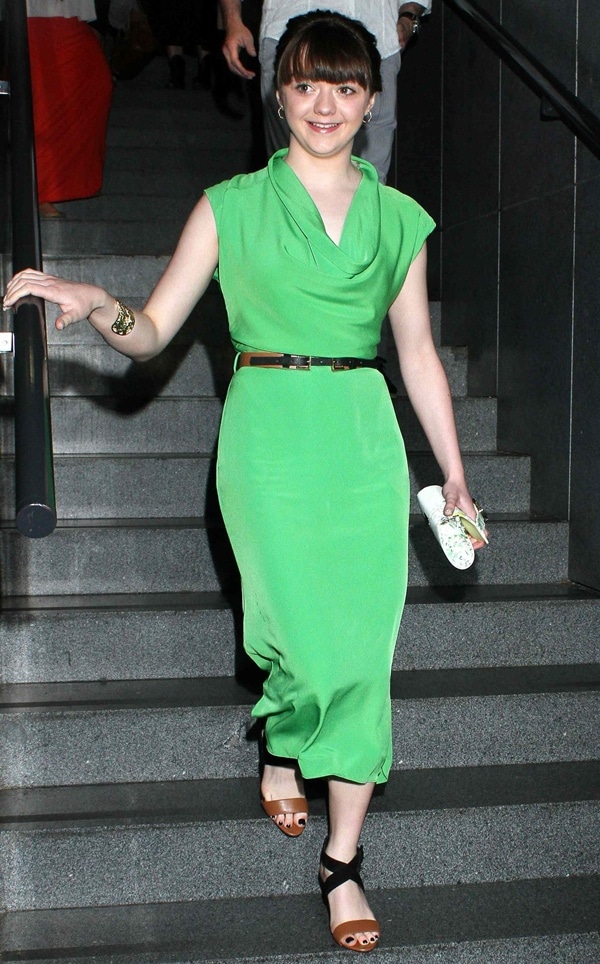 Maisie Williams's early style showcased: a green cowl-neck dress, styled with a utilitarian belt and a bold gold cuff