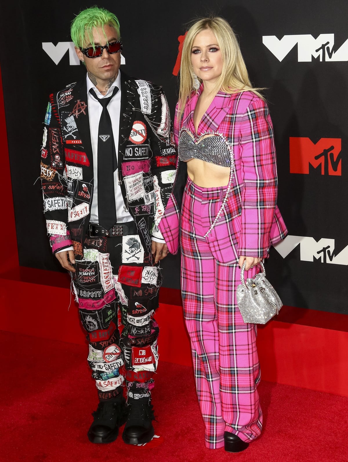 Avril Lavigne embraces her Y2K edge in a hot-pink plaid Area Pre-Fall 2021 suit paired with a crystal-studded bandeau top, platform Stuart Weitzman shoes, and a sparkly Jimmy Choo “Bon Bon” bag—joined by Mod Sun in punk-patched separates
