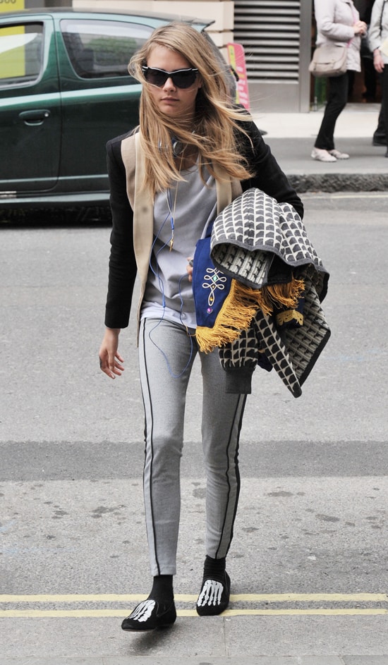 Cara Delevingne exudes casual chic in two-tone leggings, skeleton-print Mara Mine slippers, and Lulu Guinness sunglasses, layering effortlessly for a bold street style