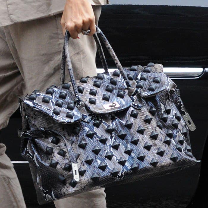 Her statement Birkin—crafted in gray snakeskin and covered in bold pyramid studs—turns a classic travel tote into a high-impact accessory, contrasting sharply with her understated neutral suit